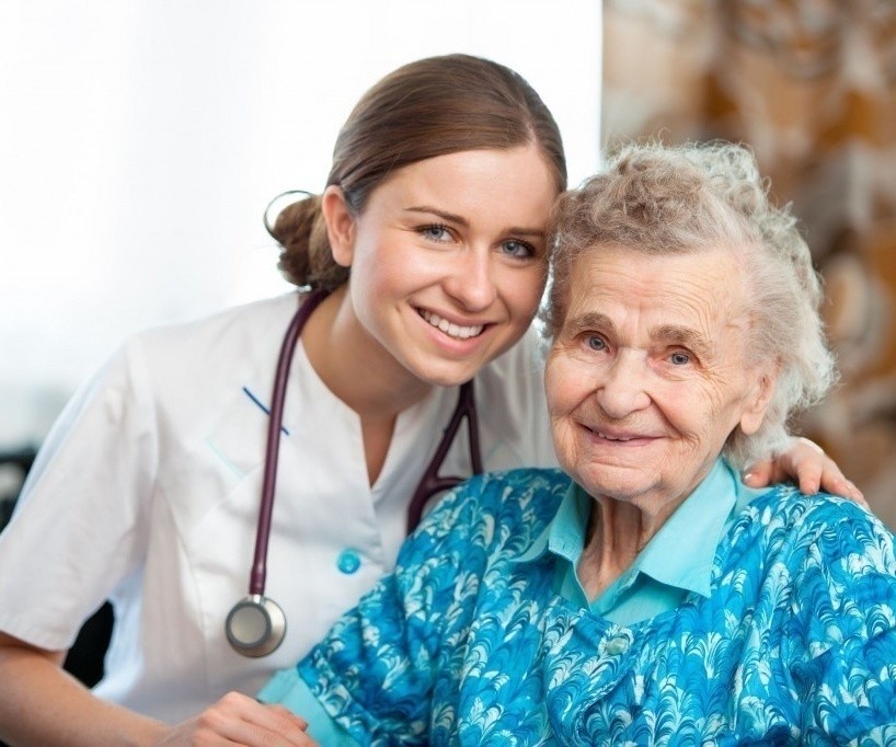 A smiling nurse with her arm around an older woman